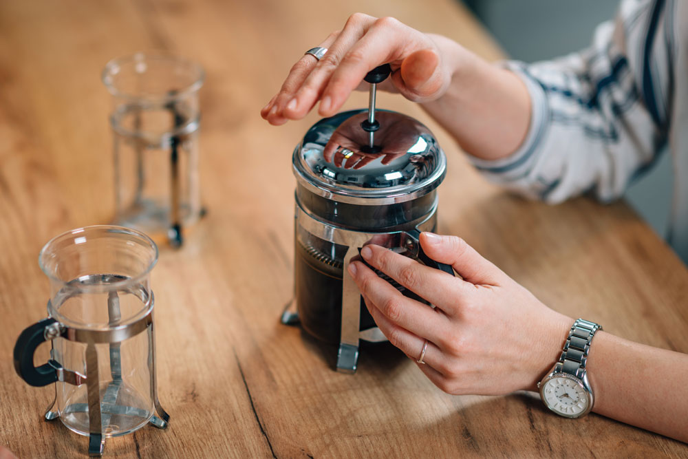Person using french press on wooden counter top 