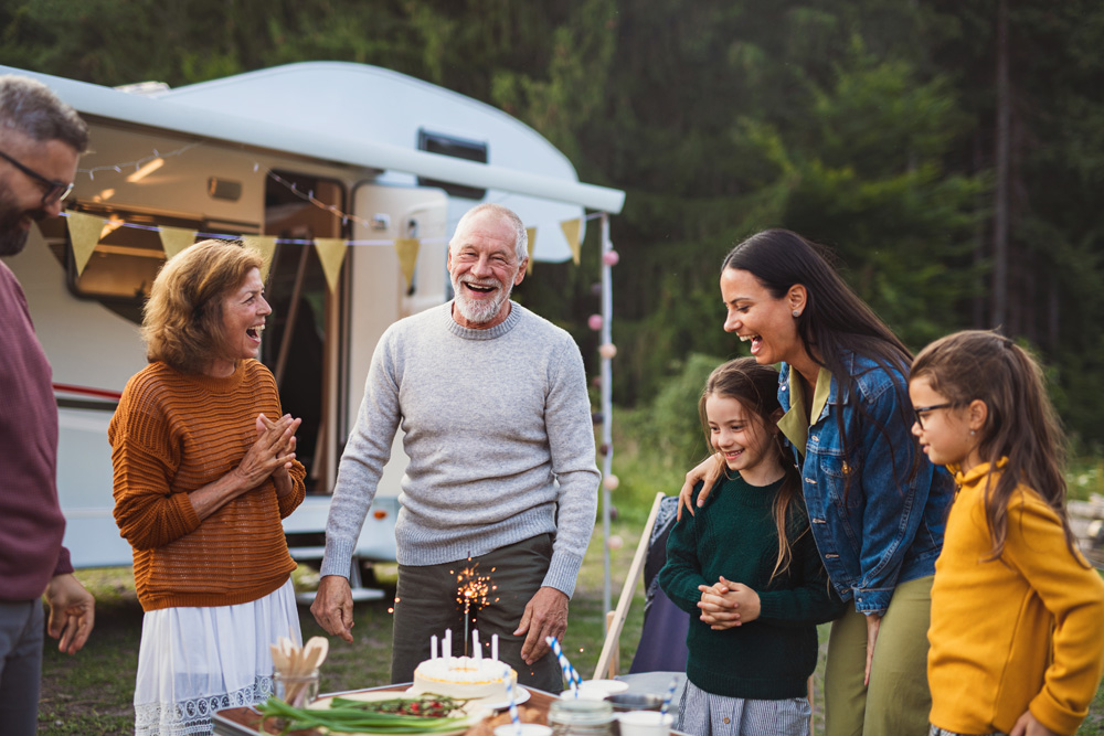 Multi generational family celebrating a birthday outside their RV in the woods